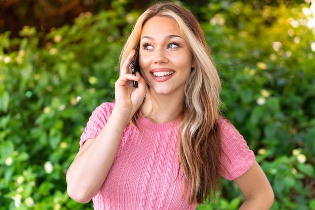 誰かと携帯電話で会話をしている屋外で若いきれいな女性