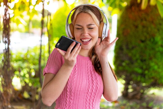 Young pretty woman at outdoors listening music with a mobile and singing