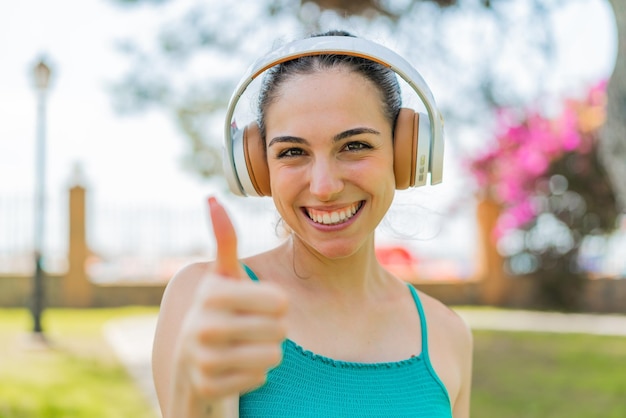 Young pretty woman at outdoors listening music and with thumb up