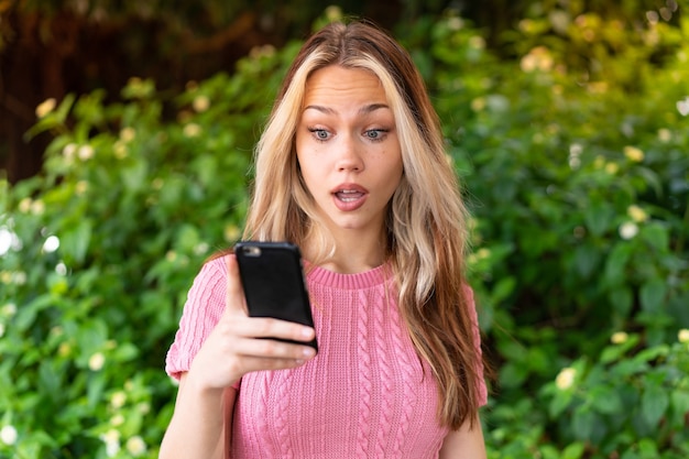 携帯電話でメッセージやメールを送信する屋外で若いきれいな女性
