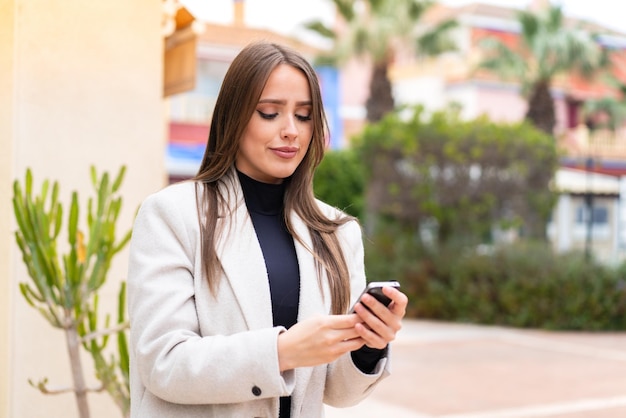 携帯電話でメッセージやメールを送信する屋外で若いきれいな女性