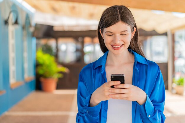 Foto giovane donna graziosa all'aperto che invia un messaggio o un'e-mail con il cellulare