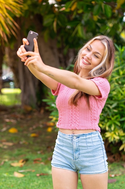 Young pretty woman at outdoors using mobile phone and doing a selfie