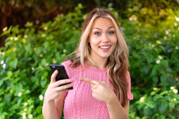 Young pretty woman at outdoors using mobile phone and pointing it