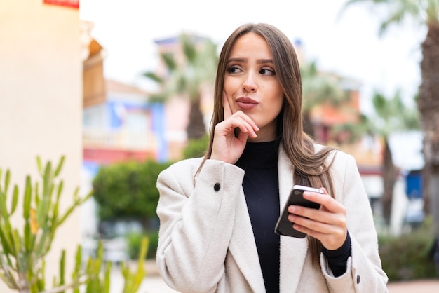 Young pretty woman at outdoors using mobile phone and thinking