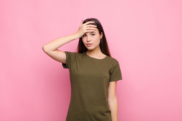 Young pretty woman panicking over a forgotten deadline, feeling stressed, having to cover up a mess or mistake against pink wall