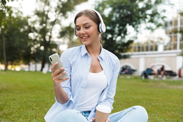 Young pretty woman in park outdoors listening music using mobile phone.