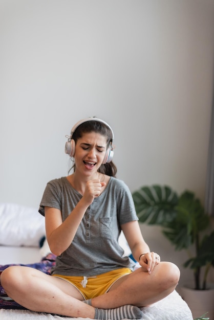 La giovane donna graziosa è felice e si diverte con la musica usando l'auricolare per ascoltare un audio audio in camera da letto a casa rilassarsi e divertirsi con uno stile di vita divertente con un concetto di cuffia per l'intrattenimento della casa della melodia della canzone