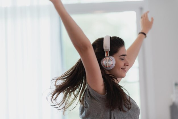 La giovane donna graziosa è felice e si diverte con la musica usando l'auricolare per ascoltare un audio audio in camera da letto a casa rilassarsi e divertirsi con uno stile di vita divertente con un concetto di cuffia per l'intrattenimento della casa della melodia della canzone