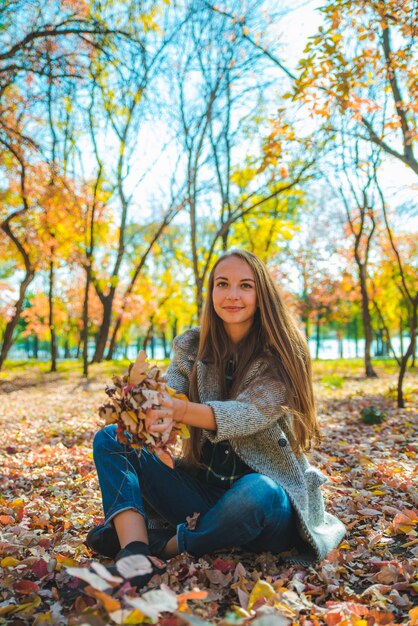 Young pretty woman playing with yellow autumn leaves at city park