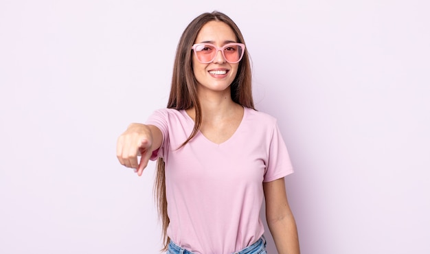 Giovane donna graziosa che punta alla telecamera scegliendo te. concetto di occhiali da sole rosa
