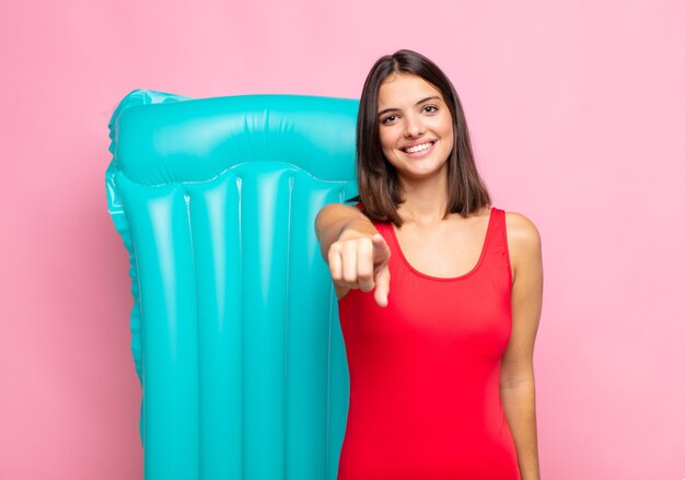 Giovane bella donna che punta alla telecamera con un sorriso soddisfatto, fiducioso, amichevole, scegliendo te