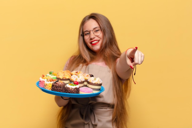 Young pretty woman. pointing gesture baker with cupcakes