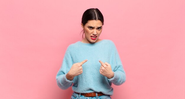 young pretty woman pointing to self with a confused and quizzical look, shocked and surprised to be chosen