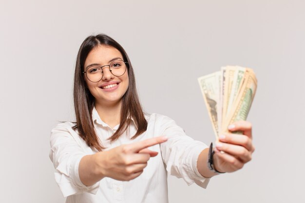 Молодая красивая женщина указывает или показывает и держит долларовые банкноты