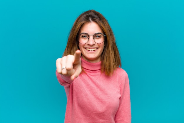 Foto giovane donna graziosa che indica con un sorriso soddisfatto, sicuro, amichevole, scegliendovi contro la parete blu