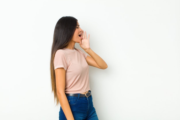 Vista di profilo di giovane donna graziosa, guardando felice ed eccitato, gridando e chiamando per copiare lo spazio sul lato contro il muro