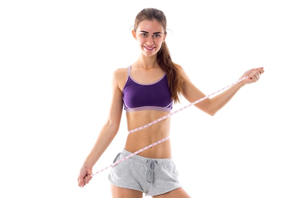 Young pretty woman in purple sports top with ponytail using centimeter on white background in studio