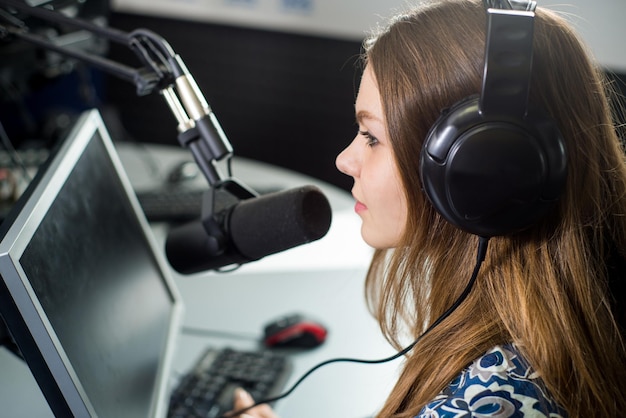 Young pretty woman radio presenter sitting in studio with\
headphones and talking on the air