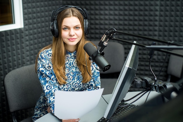 Young pretty woman radio presenter sitting in studio with\
headphones and talking on the air