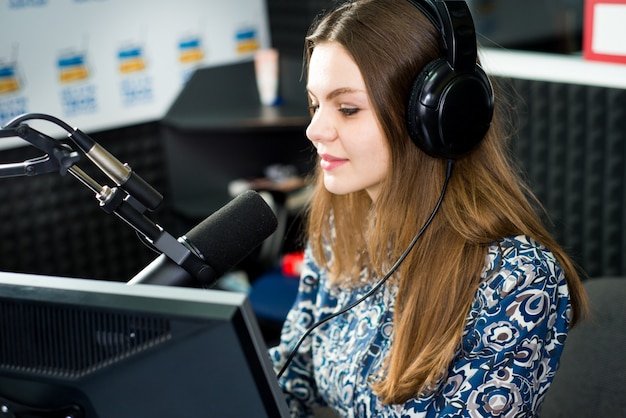 Young pretty woman radio presenter sitting in studio with headphones and talking on the air