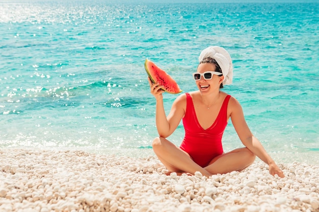 Young pretty woman in red swimsuit at the beach holding watermelon copy space