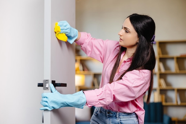 A young pretty woman in rubber gloves wipes the door with a rag