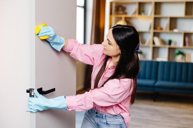 A young pretty woman in rubber gloves wipes the door with a rag