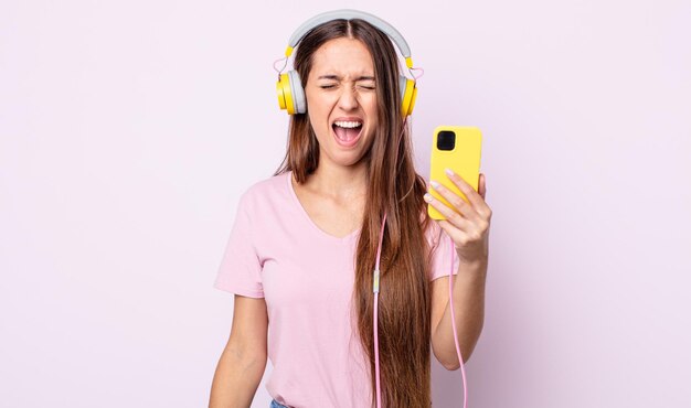 Young pretty woman shouting aggressively, looking very angry. headphones and smartphone