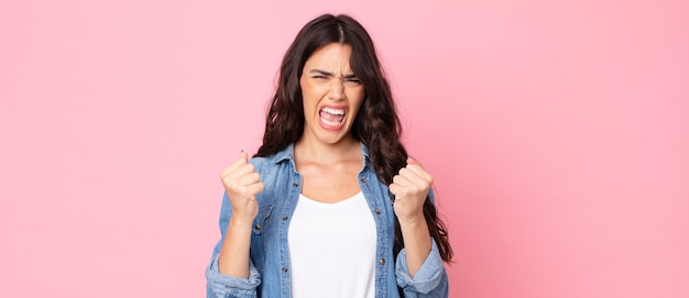 young pretty woman shouting aggressively with annoyed, frustrated, angry look and tight fists, feeling furious