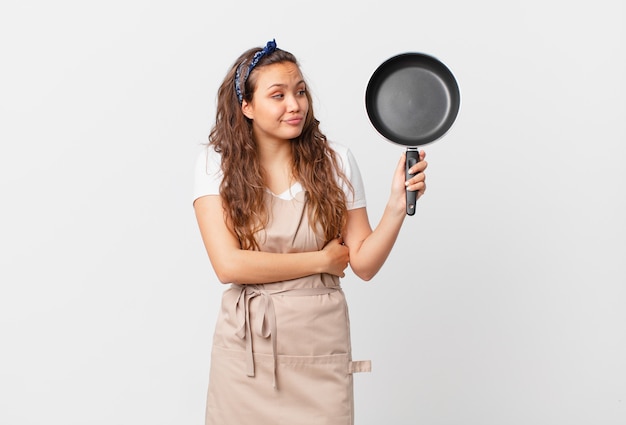 Young pretty woman shrugging, feeling confused and uncertain chef concept and holding a pan