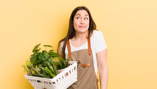 混乱して不確かな植物の概念を肩をすくめる若いきれいな女性