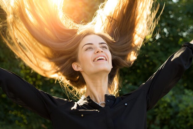 Young pretty woman in and silver necklace throwing up her long chestnut hair of  bright sunlight