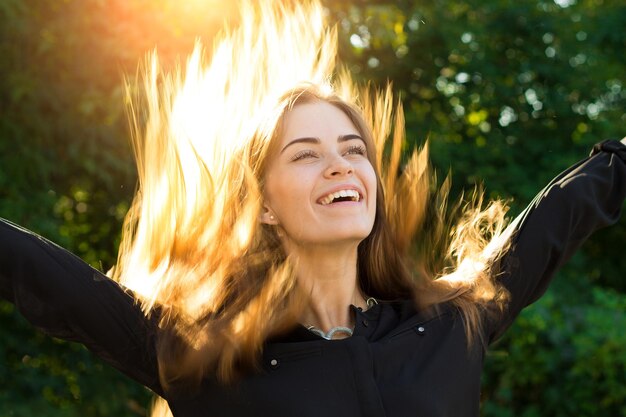 Young pretty woman in and silver necklace throwing up her long chestnut hair of  bright sunlight