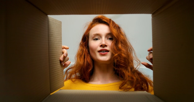 Young pretty woman sitting on couch in living room and opening carton box