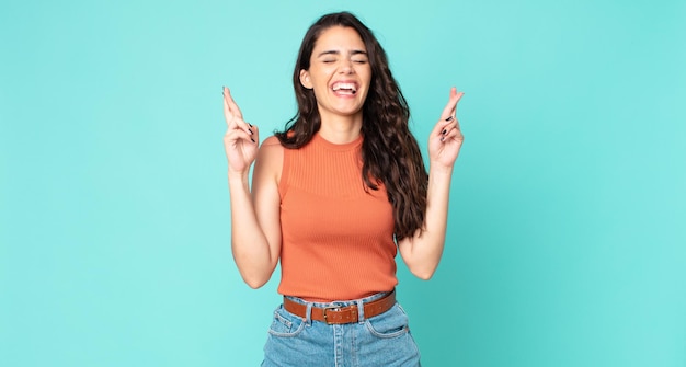若いきれいな女性の笑みを浮かべて、両方の指を心配そうに交差、心配と希望または幸運を願って感じ