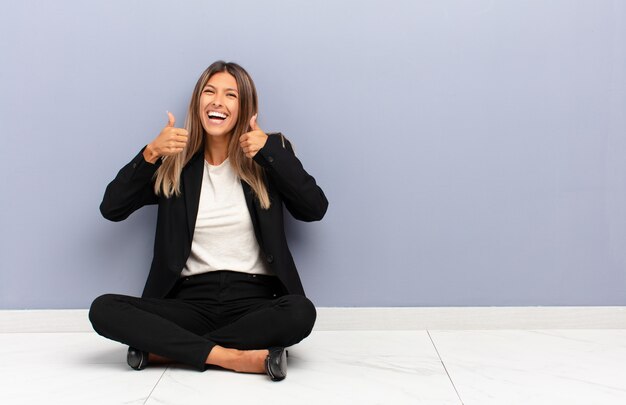 Young pretty woman smiling broadly looking happy, positive, confident and successful, with both thumbs up business concept