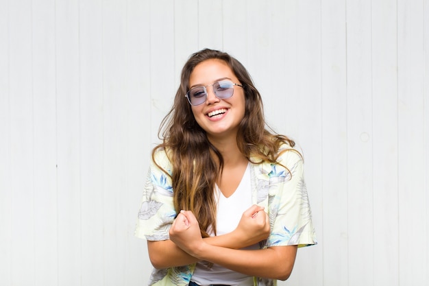 Young pretty woman smiling cheerfully and celebrating, with fists clenched and arms crossed, feeling happy and positive