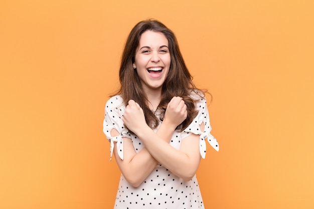 Young pretty woman smiling cheerfully and celebrating, with fists clenched and arms crossed