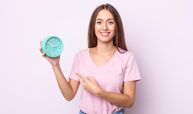 Young pretty woman smiling cheerfully, feeling happy and pointing to the side. alarm clock concept