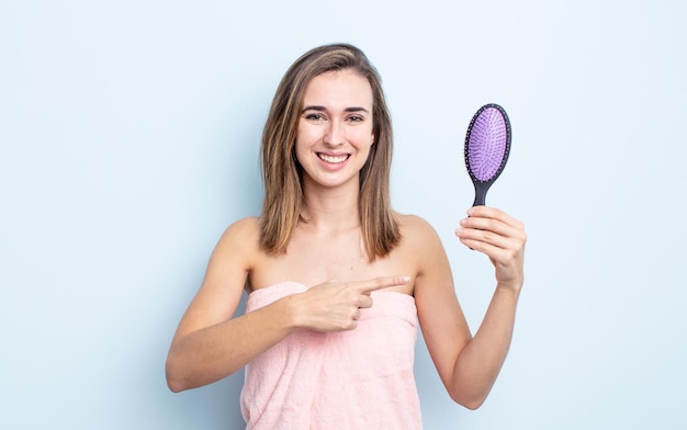 元気に笑って、幸せを感じて、横を指している若いきれいな女性。ヘアブラシのコンセプト