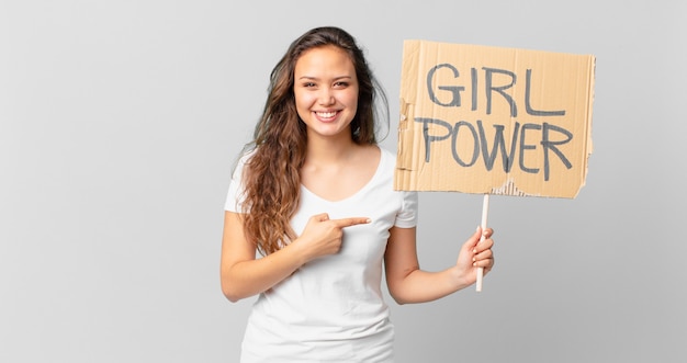 Young pretty woman smiling cheerfully, feeling happy and pointing to the side and holding a girl power banner