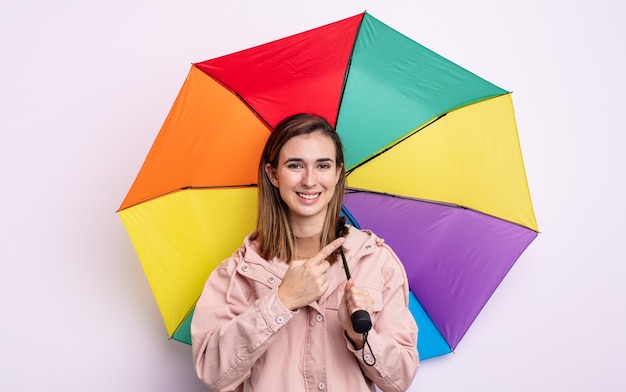 Young pretty woman smiling cheerfully, feeling happy and pointing to the side. umbrella concept