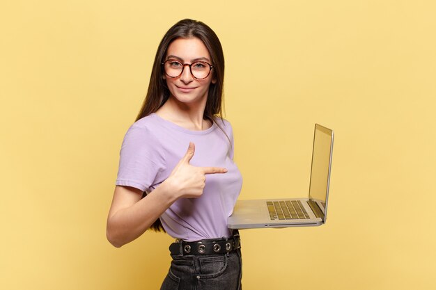 Young pretty woman smiling cheerfully, feeling happy and pointing to the side and upwards, showing object in copy space. laptop concept