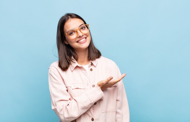 Young pretty woman smiling cheerfully, feeling happy and showing a concept in copy space with palm of hand