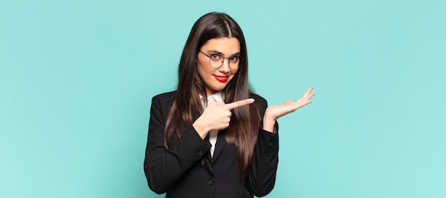 Young pretty woman smiling cheerfully and pointing to copy space on palm on the side, showing or advertising an object. business concept