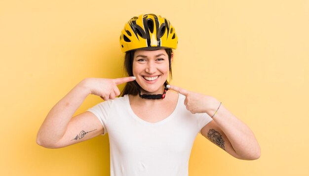 Young pretty woman smiling confidently pointing to own broad smile bike helmet concept