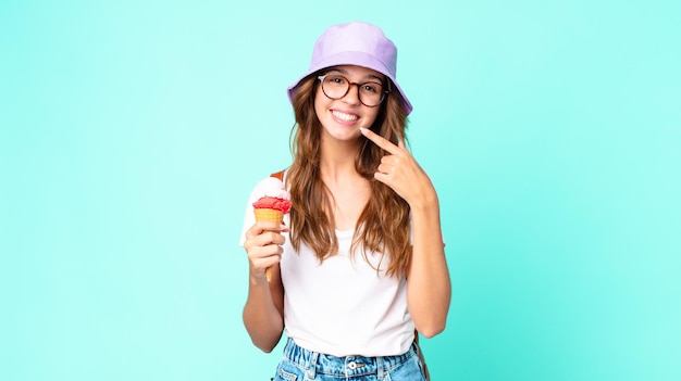 Giovane donna graziosa che sorride con sicurezza indicando il proprio ampio sorriso che tiene in mano un gelato. concetto di estate