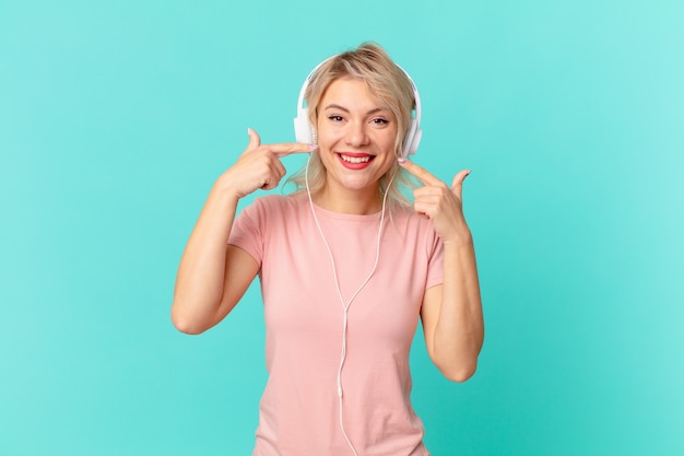 Giovane donna graziosa che sorride con sicurezza indicando il proprio ampio sorriso. ascoltando il concetto di musica