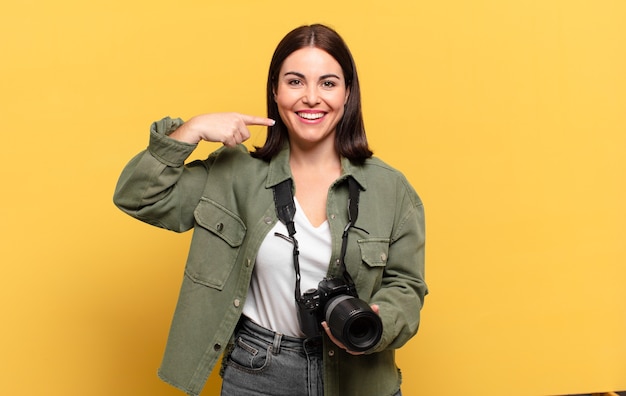 Young pretty woman smiling confidently pointing to own broad smile, positive, relaxed, satisfied attitude